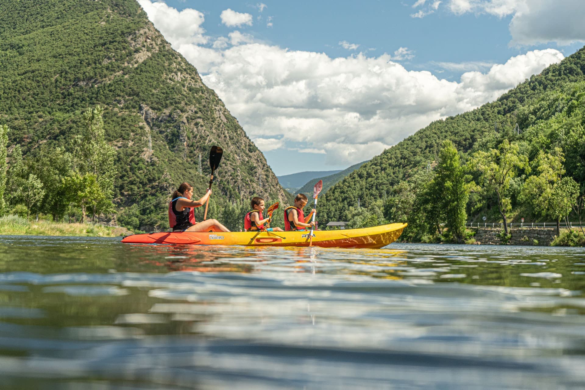 Varias personas navegando en kayaks individuales y dobles por las aguas tranquilas del lago de La Torrassa, rodeados de vegetación.