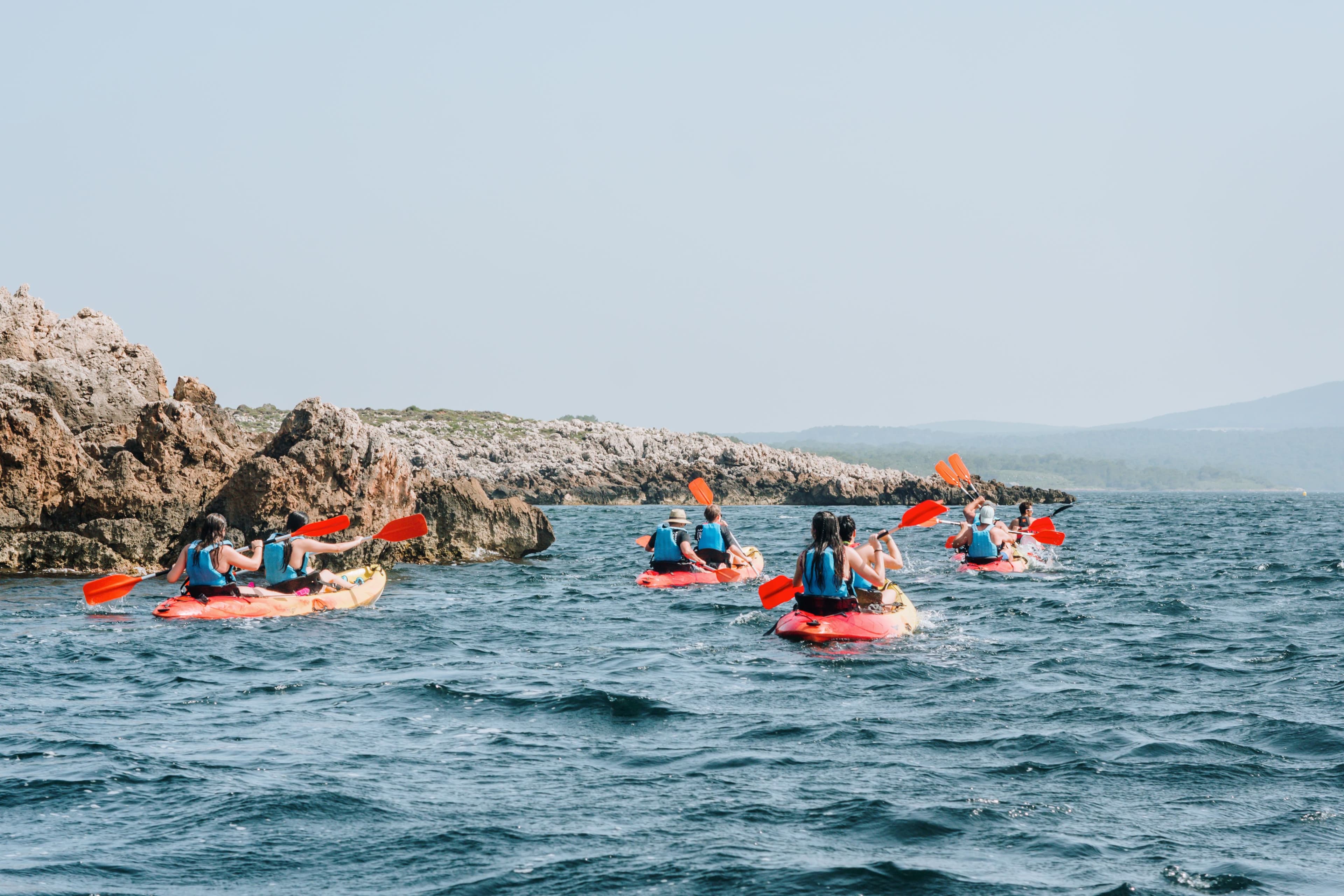 Grupo de kayakistas equipados con máscaras de snorkel descansando junto a sus embarcaciones en una cala de aguas turquesas en Menorca.