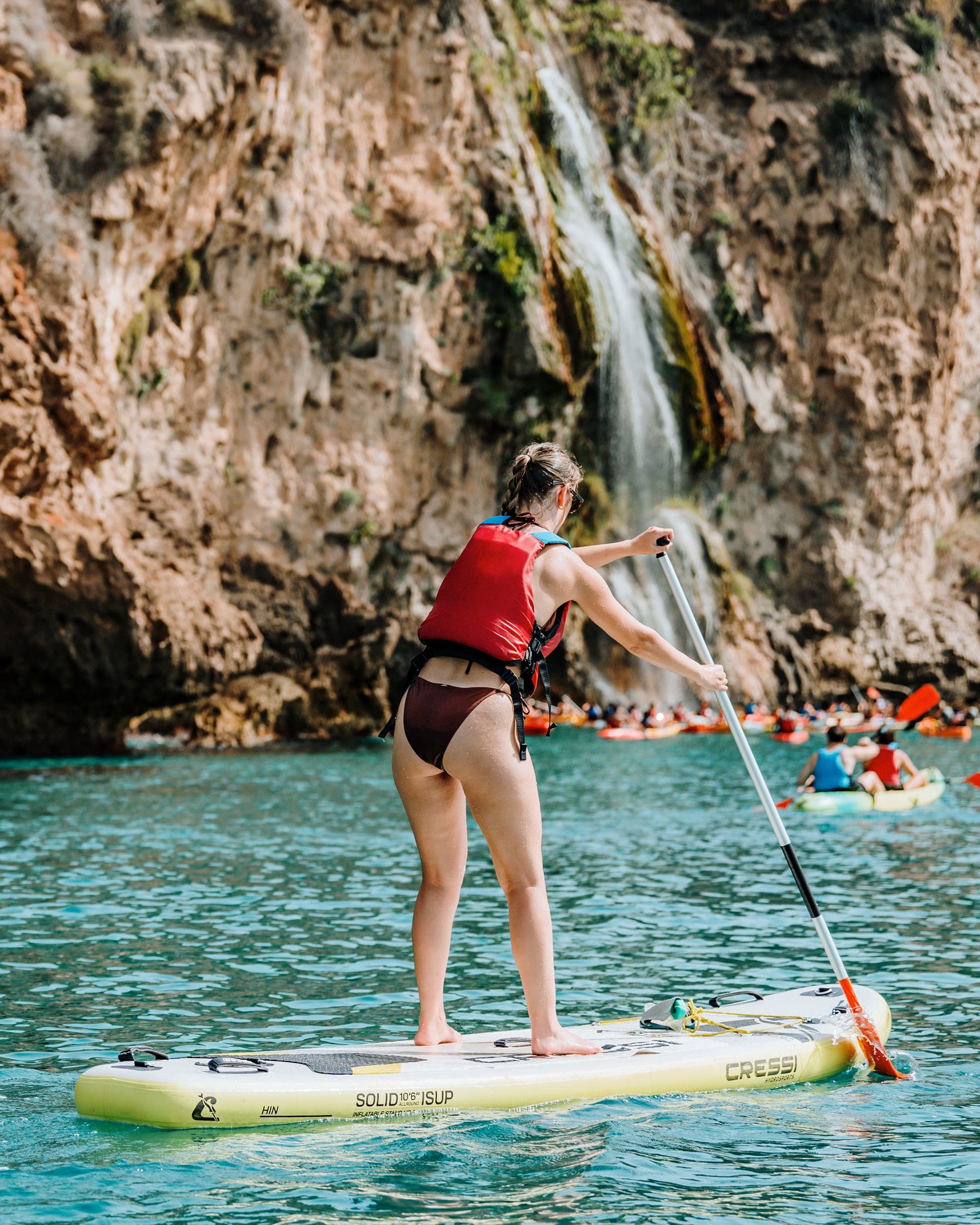 Persona practicando paddle surf frente a la Cascada de Maro en los acantilados de Nerja.