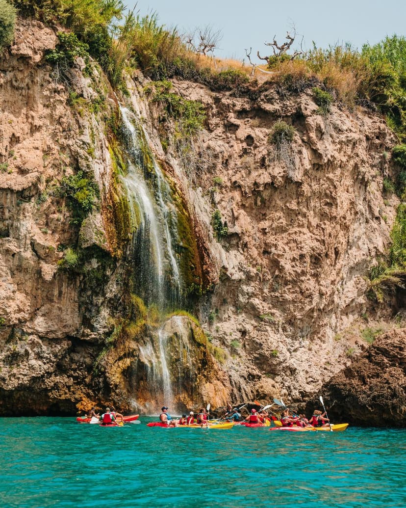 Grupo de personas en kayak navegando cerca de la Cascada de Maro en los acantilados de Nerja.