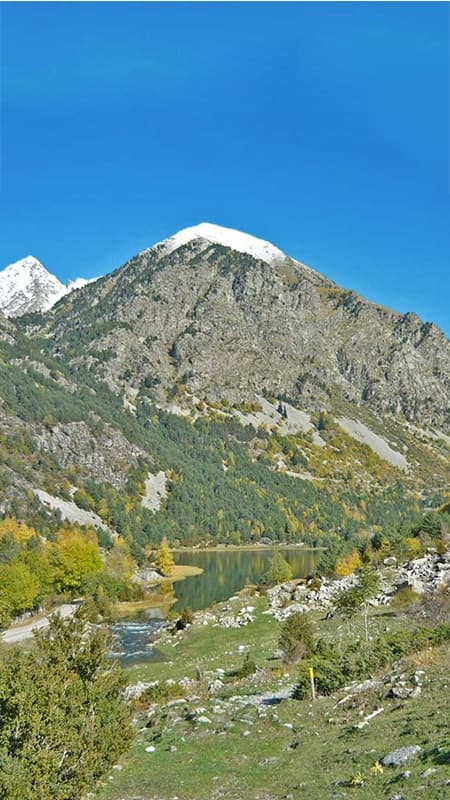 Senderistas caminando por un sendero de alta montaña frente a los meandros del Parque Nacional de Aigüestortes.