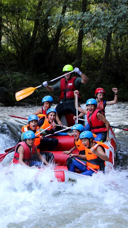 Grupo de personas con casco y chaleco remando en una balsa de rafting por los rápidos del río Noguera Ribagorçana.